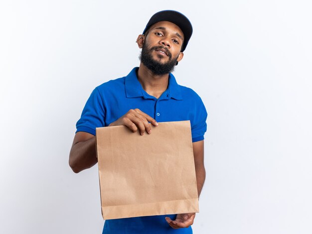 Zelfverzekerde jonge Afro-Amerikaanse bezorger die een voedselpakket vasthoudt dat op een witte muur met kopieerruimte wordt geïsoleerd