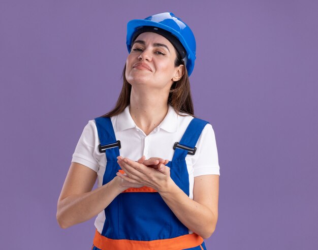 Zelfverzekerde jonge bouwer vrouw in uniform hand in hand samen geïsoleerd op paarse muur