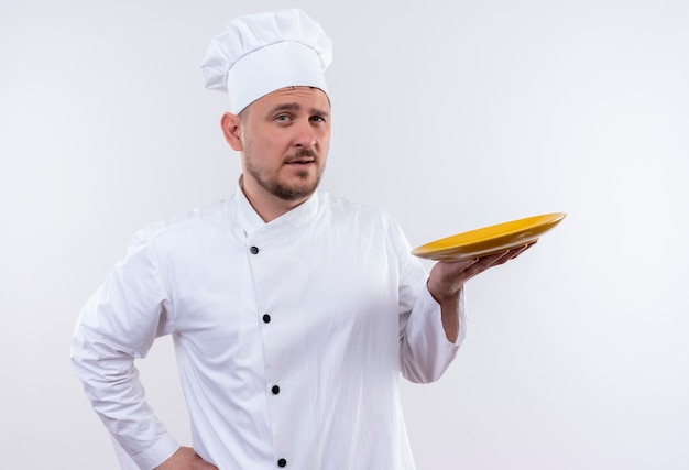 Zelfverzekerde jonge knappe kok in uniform met chef-kok bord op geïsoleerde witte muur