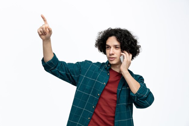 Zelfverzekerde jonge knappe man kijkend naar kant praten over telefoon wijzende vinger omhoog geïsoleerd op witte achtergrond