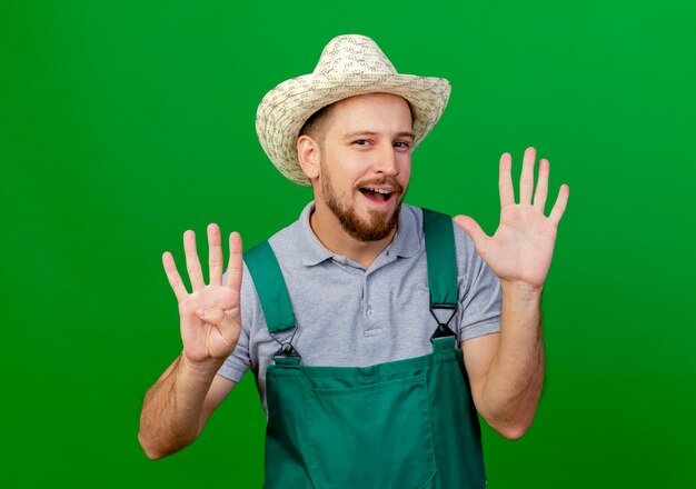 Zelfverzekerde jonge knappe Slavische tuinman in uniform en hoed op zoek met lege handen