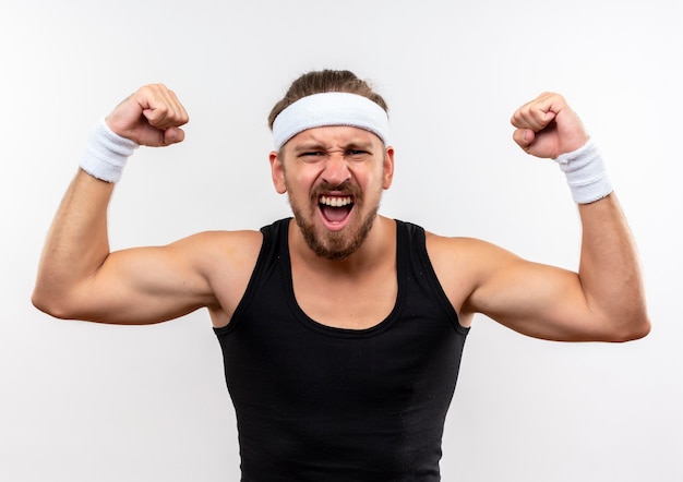 Zelfverzekerde jonge knappe sportieve man met hoofdband en polsbandjes gebaren sterk geïsoleerd op een witte muur