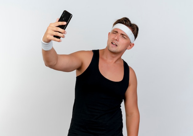 Zelfverzekerde jonge knappe sportieve man met hoofdband en polsbandjes nemen selfie geïsoleerd op wit
