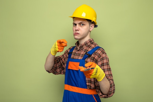 Zelfverzekerde jonge mannelijke bouwer die uniform draagt met handschoenen die een steeksleutel vasthouden