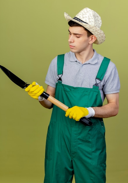 Zelfverzekerde jonge mannelijke tuinman met een tuinhoed houdt vast en kijkt naar spade