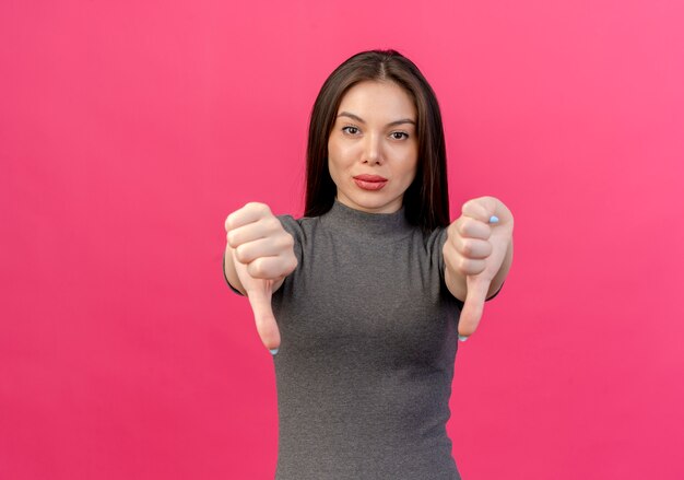 Zelfverzekerde jonge mooie vrouw duimen omlaag geïsoleerd op roze achtergrond met kopie ruimte tonen