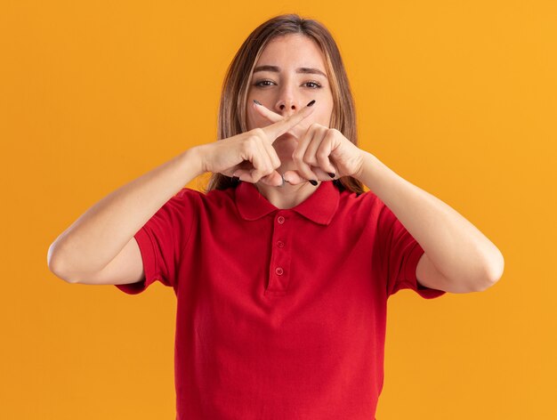 Zelfverzekerde jonge mooie vrouw kruist vingers gebaren geen teken geïsoleerd op oranje muur