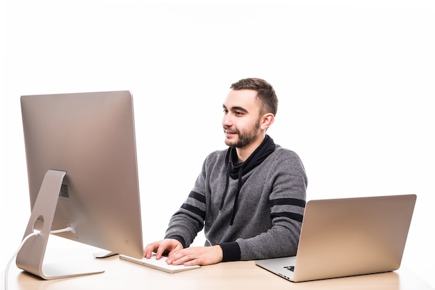 Zelfverzekerde jonge ondernemer zittend aan de tafel met laptop en pc geïsoleerd op wit