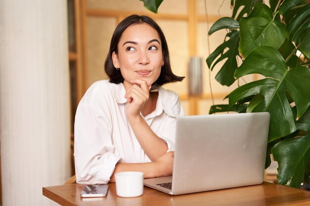 Zelfverzekerde jonge stijlvolle vrouw met laptop zittend in café en werkende freelancer in coworking-ruimte