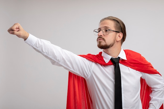 Gratis foto zelfverzekerde jonge superheld man kijken kant dragen medische mantel met een stethoscoop en een bril verhogen hand geïsoleerd op een witte achtergrond