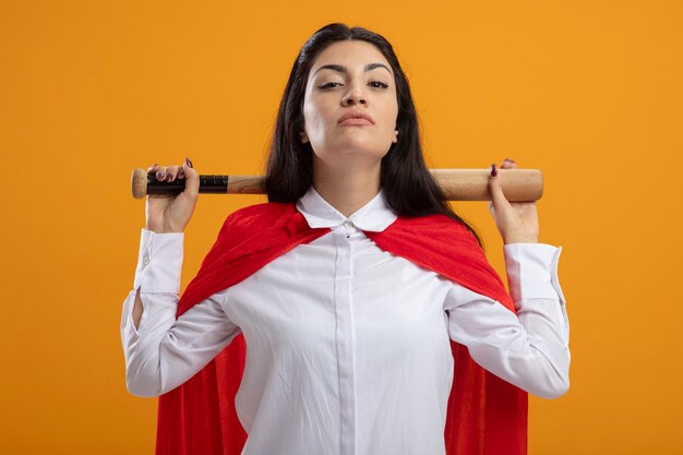 Zelfverzekerde jonge superwoman met honkbalknuppel achter nek kijken voorzijde geïsoleerd op oranje muur
