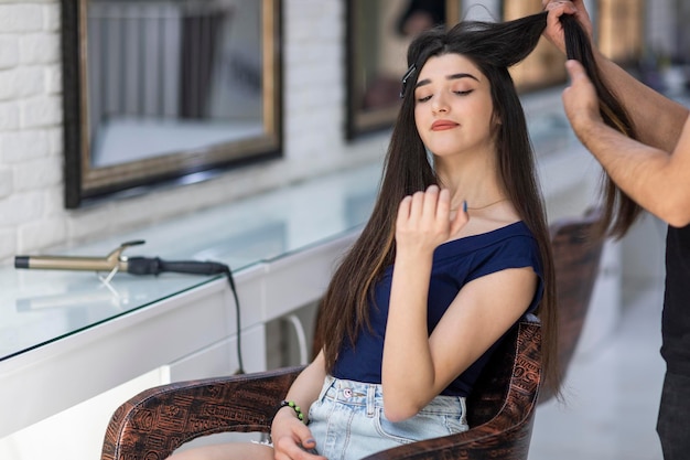 Zelfverzekerde jonge vrouw die bij de kapper zit en naar haar hand kijkt hoge kwaliteit foto