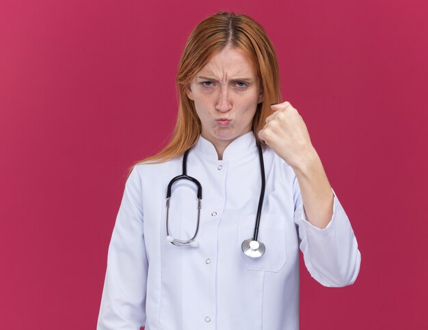 Zelfverzekerde jonge vrouwelijke gemberdokter die medische mantel en stethoscoop draagt, doet een sterk gebaar
