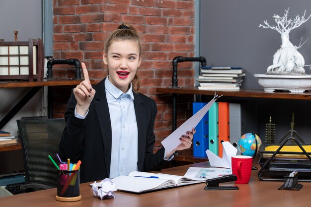 Zelfverzekerde jongedame die aan een tafel zit en het document omhoog houdt op kantoor