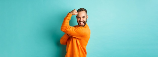 Zelfverzekerde knappe man pronkt met zijn spieren flex biceps en voelt zich sterk staande over lichtblauwe backg