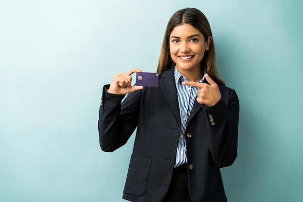 Zelfverzekerde knappe vrouwelijke ondernemer wijzend op haar creditcard tegen geïsoleerde achtergrond
