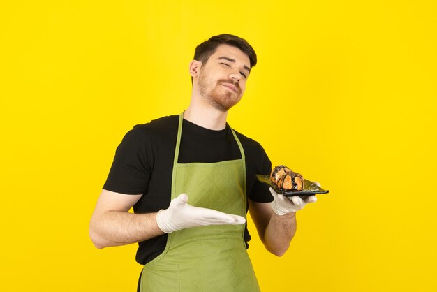 Zelfverzekerde man die cakeplak vasthoudt en met de hand op een geel laat zien