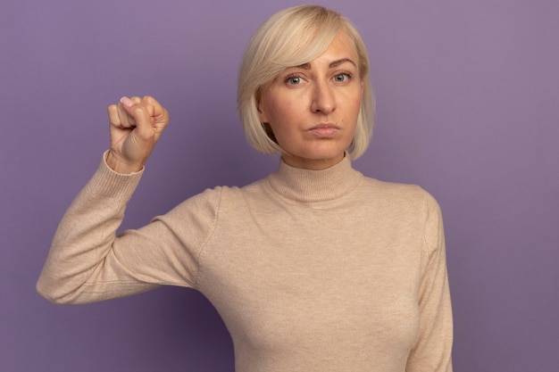 Gratis foto zelfverzekerde mooie blonde slavische vrouw houdt vuist op paars