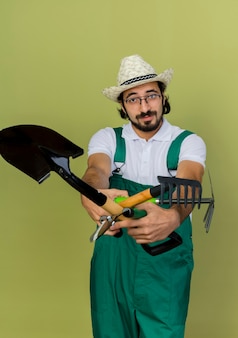 Zelfverzekerde tuinman met een optische bril die een tuinhoed draagt, houdt tuingereedschap vast