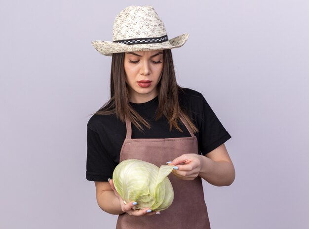 Zelfverzekerde, vrij blanke vrouwelijke tuinman met een tuinhoed die vasthoudt en naar kool kijkt