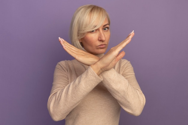 Gratis foto zelfverzekerde vrij blonde slavische vrouw die handen kruist die geen teken op paars gebaren