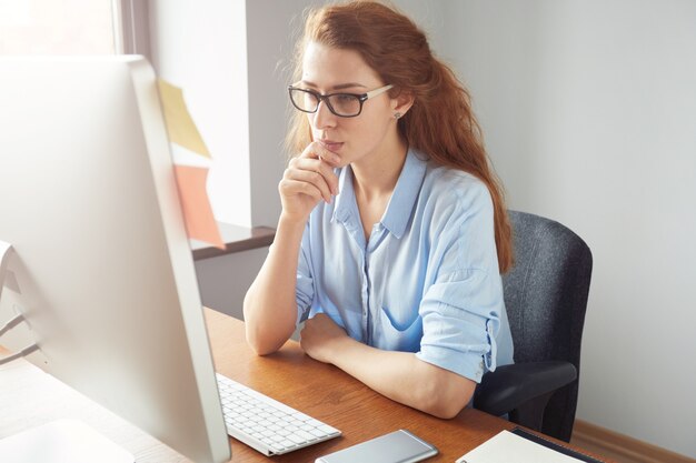 Zelfverzekerde vrouwelijke freelancer zit achter de computer met ernstige en doordachte uitdrukking