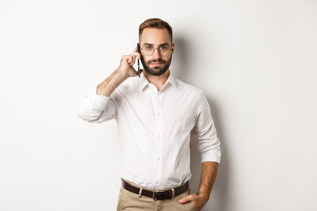 Zelfverzekerde zakenman praten aan de telefoon, serieus kijken, staan