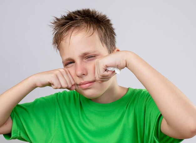 Ziek jongetje in groen t-shirt gevoel onwel zijn ogen staande over witte achtergrond