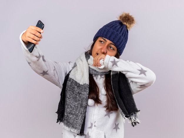 Ziek meisje met winter hoed met sjaal neemt een selfie geïsoleerd op een witte achtergrond