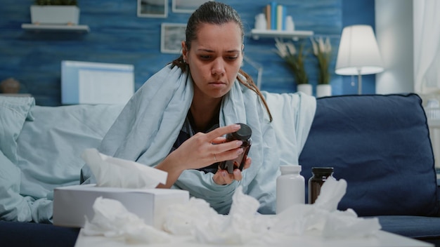 Ziek volwassen leesetiket van fles met pillen en tablet met capsules op zoek naar behandeling om ziekte en griep te genezen. Zieke vrouw die medicijnflessen bekijkt voor remedie en gezondheidszorg