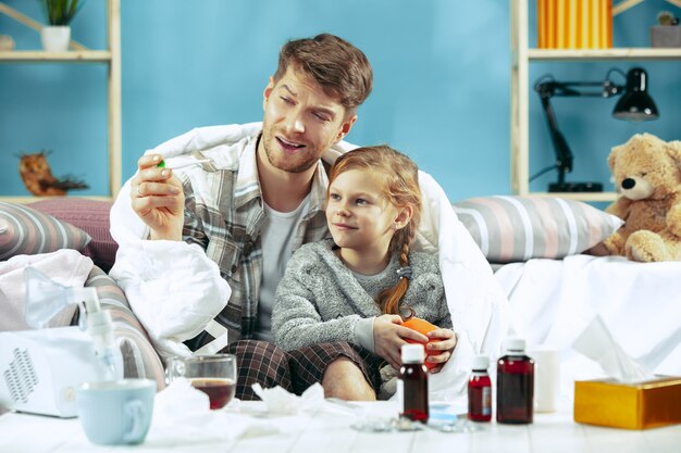 Zieke man met dochter thuis. Thuisbehandeling. Vechten met een ziekte. Medische gezondheidszorg. Familieleden. De winter, griep, gezondheid, pijn, ouderschap, relatieconcept. Ontspanning thuis