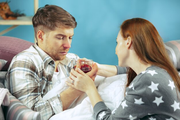 Zieke man met koorts liggend in bed met temperatuur. Zijn vrouw zorgt voor hem. De ziekte, griep, pijn, familieconcept. Ontspanning thuis