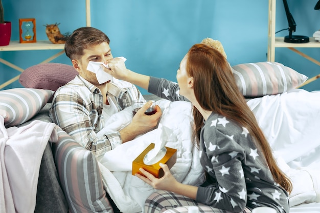 Zieke man met koorts liggend in bed met temperatuur. Zijn vrouw zorgt voor hem.