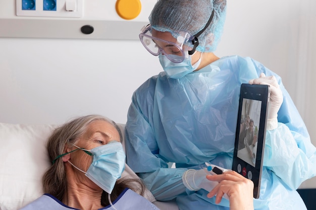 Zieke vrouwelijke patiënt in bed in het ziekenhuis in gesprek met familie via een tablet