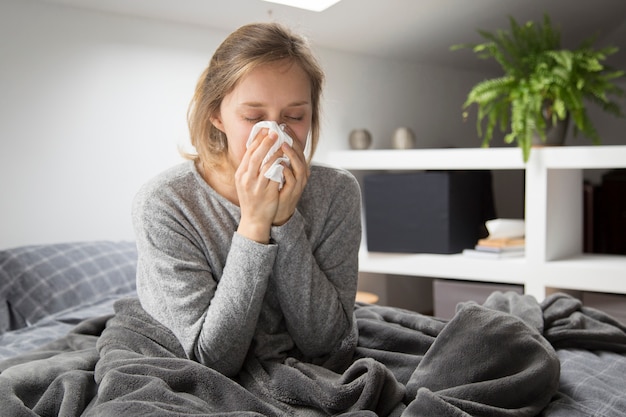 Zieke vrouwenzitting in bed, blazende neus met servet