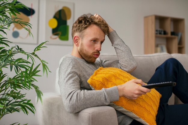 Gratis foto zijaanzicht bezorgde man op de bank tv kijken