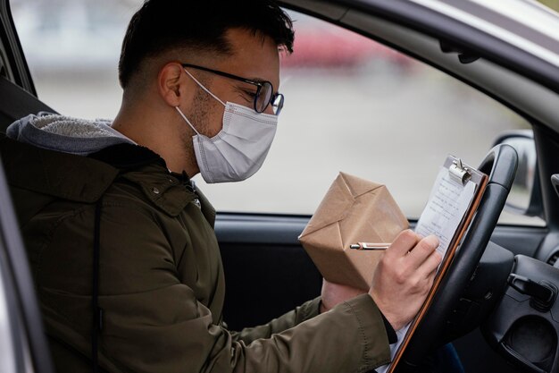 Zijaanzicht bezorger met masker in auto