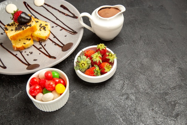 Zijaanzicht cake met chocoladetaart met chocolade en aardbeien naast de kommen met aardbeien en snoep