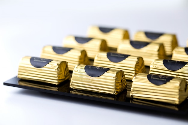 Gratis foto zijaanzicht chocoladesuikergoed in een gouden wikkel op zwarte standaard