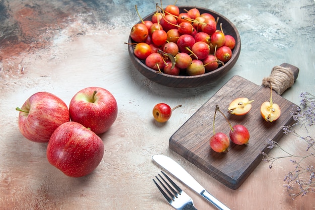 Zijaanzicht close-up kersen vork mes kersen in de kom en op het bord drie appels