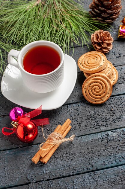 Zijaanzicht cookies Kerstkoekjes naast de kaneelstokjes een kopje thee op de schotel vuren boom met kegels en kerstspeelgoed op de houten tafel