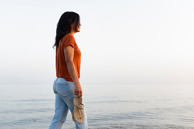 Zijaanzicht dat van peinzende vrouw een gang op het strand neemt