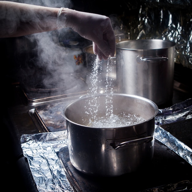 Gratis foto zijaanzicht diepe pot met kokend water en zout en menselijke hand in fornuis