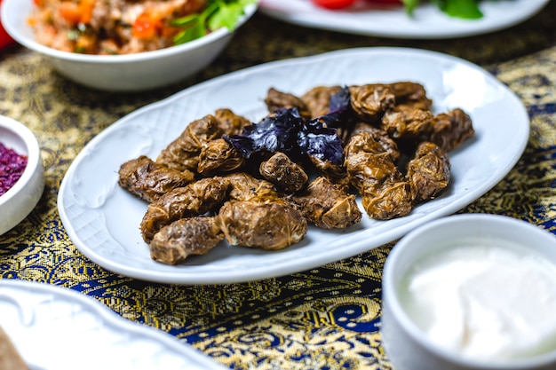 Gratis foto zijaanzicht dolma gevulde druivenbladeren met gemalen ui zout peper basilicum en yoghurt op tafel