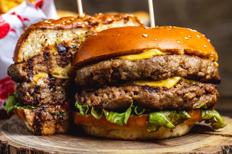 Gratis Foto zijaanzicht dubbele cheeseburger met gegrilde runderpasteitjes, kaas en slablad tussen burgerbroodjes