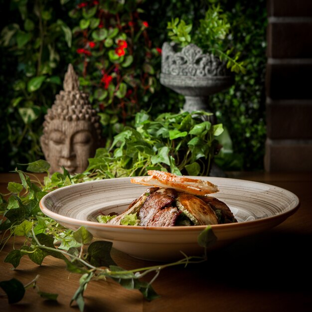 Zijaanzicht gebakken vlees met gebakken courgette en druiven tak en standbeeld hoofd in ronde plaat