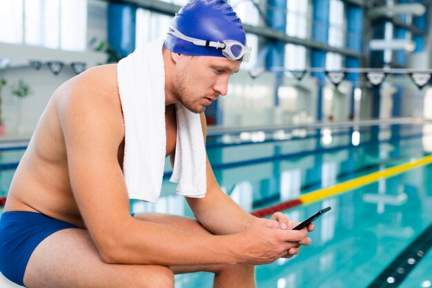 Zijaanzicht jong mannetje bij pool die telefoon met behulp van