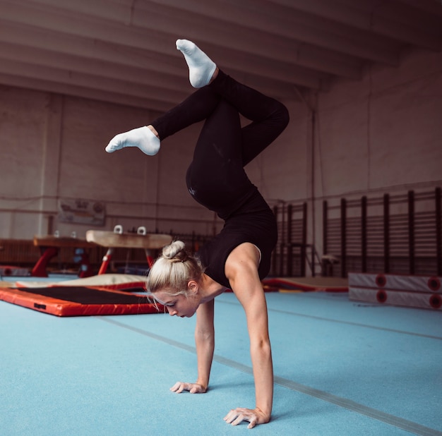 Zijaanzicht jonge blonde vrouw training voor gymnastiek kampioenschap