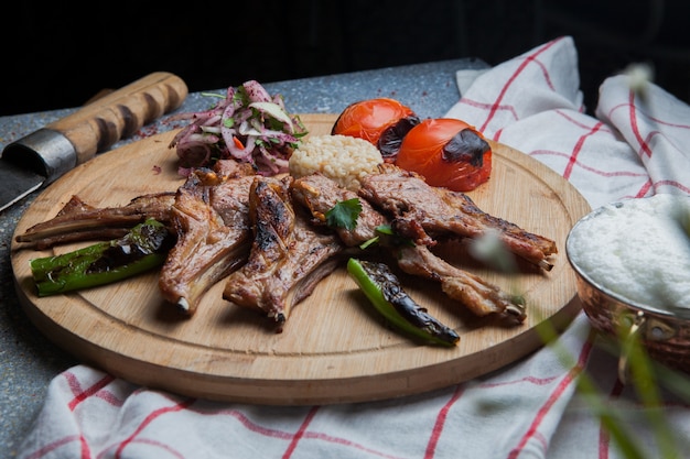 Zijaanzicht kebab ribben met gebakken groenten en gehakte ui en mes en ayran in houten voedsel lade