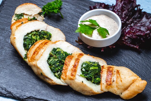 Zijaanzicht kipfilet gevuld met spinazie en saus op tafel